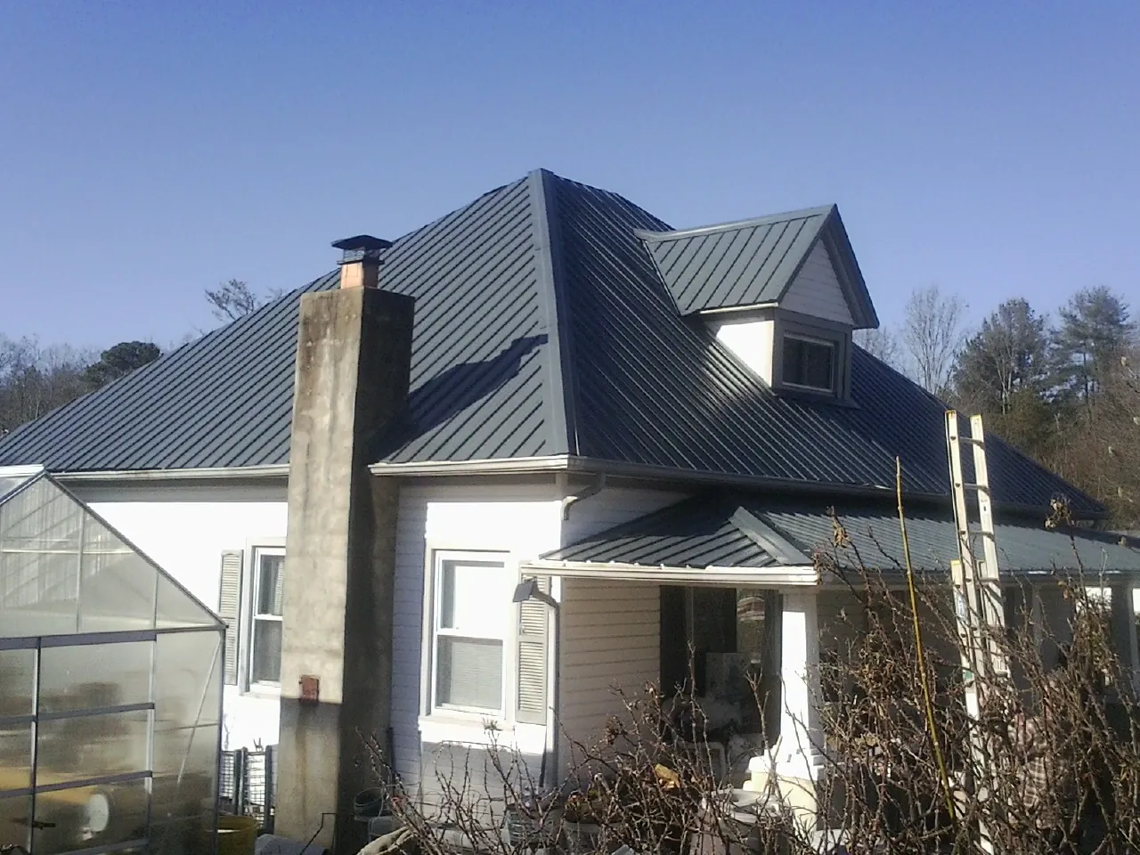 Dark blue standing seam metal roof on a white farmhouse with dormer — Slate & Tile Roof Repair by Roofing Brothers in Elton