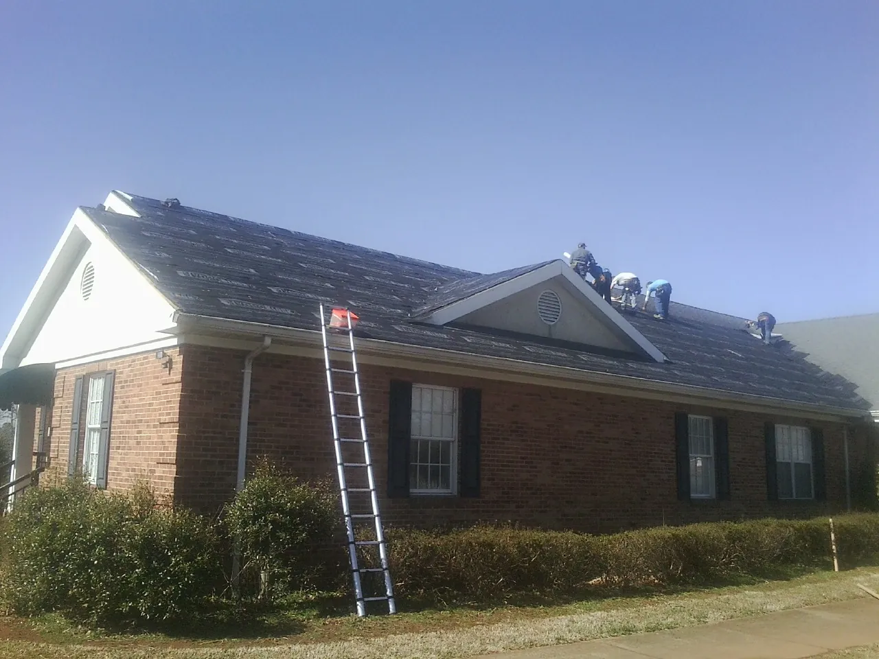 Crew tearing shingles off a brick ranch roof with a ladder set — Emergency Roof Repair work by our crew in Elton