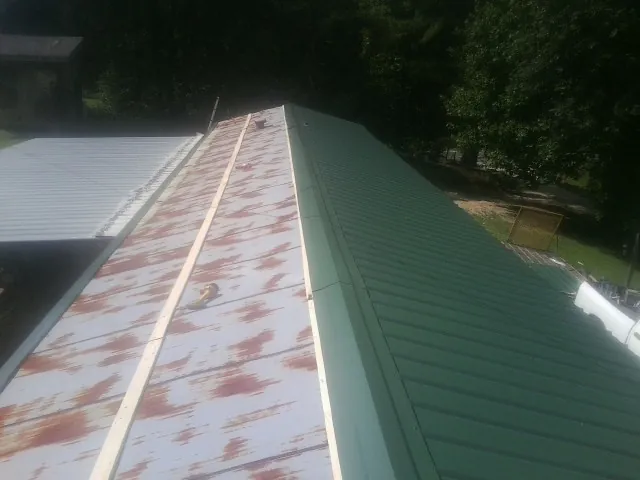 Old rusted panels beside newly installed green metal roofing — Wind Damage Roof Repair by Roofing Brothers in Elton