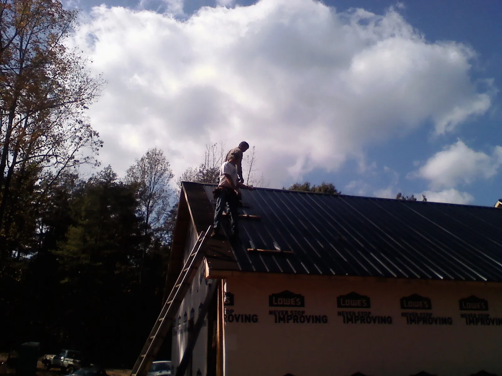 Roofer fastening dark metal panels high against a cloudy sky, from a Roof Inspection job in Elton
