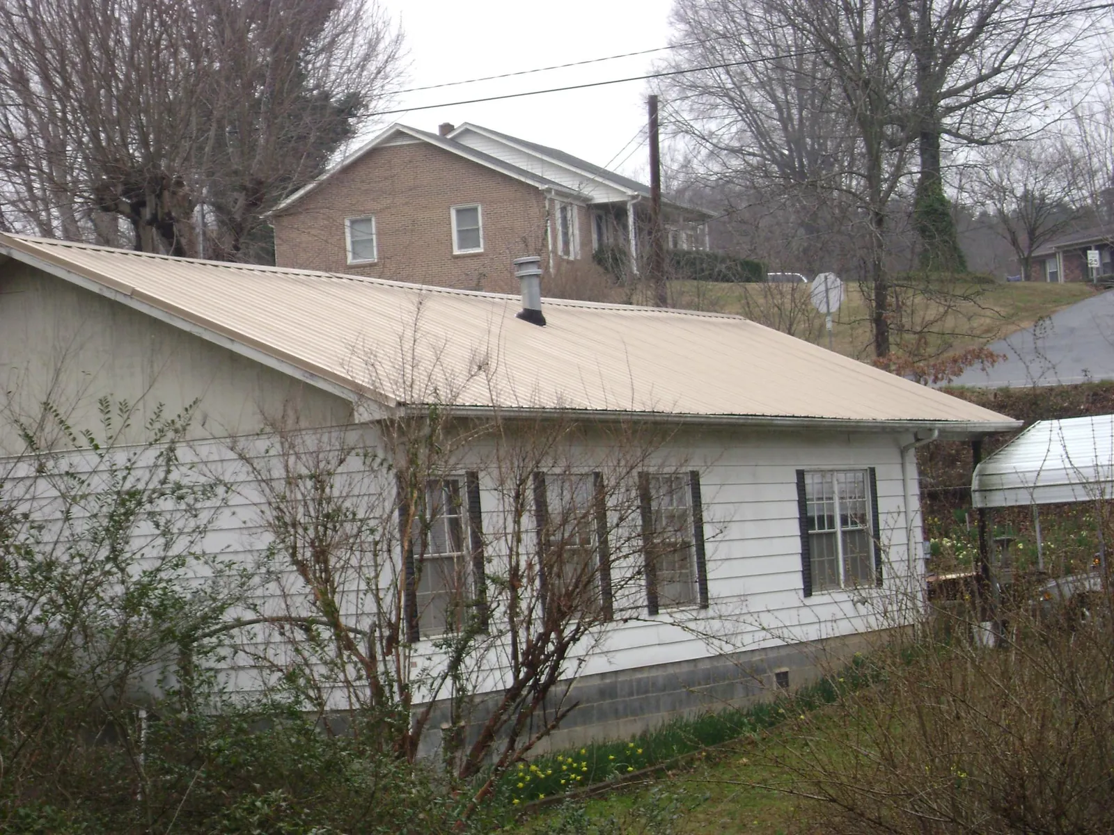 Tan metal roof on a white sided house set into a hillside — Commercial Roofing by Roofing Brothers in Elton