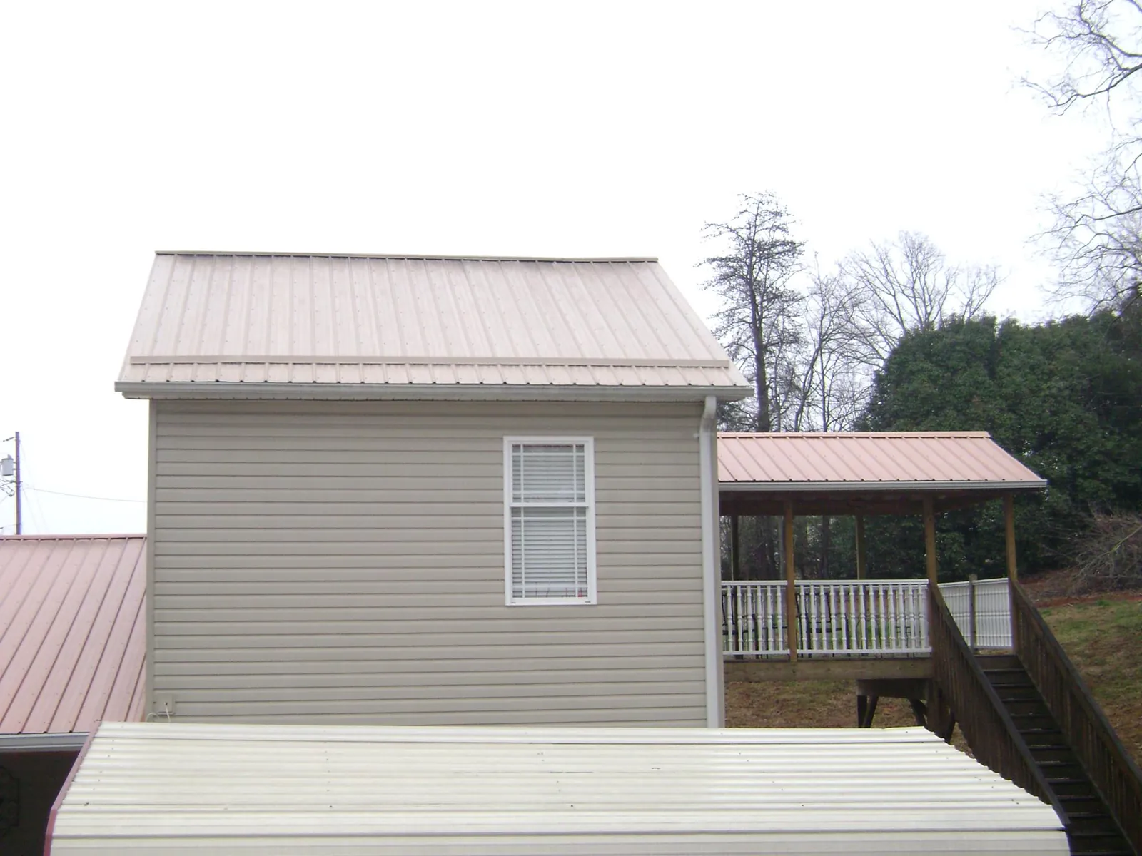 Tan metal roofs on a two story addition and attached porch, from a Roof Replacement job in Elton